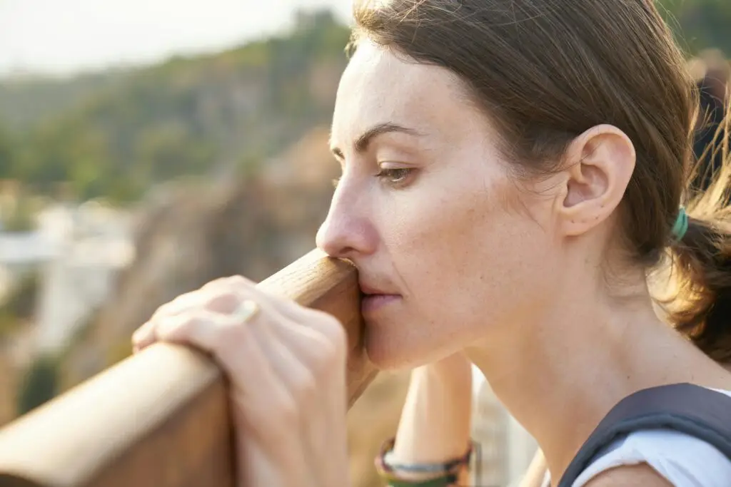 7 Signs Your Hormones are Shifting: Natural Balance After 40 A thoughtful woman leans on a railing, lost in deep contemplation outdoors.
